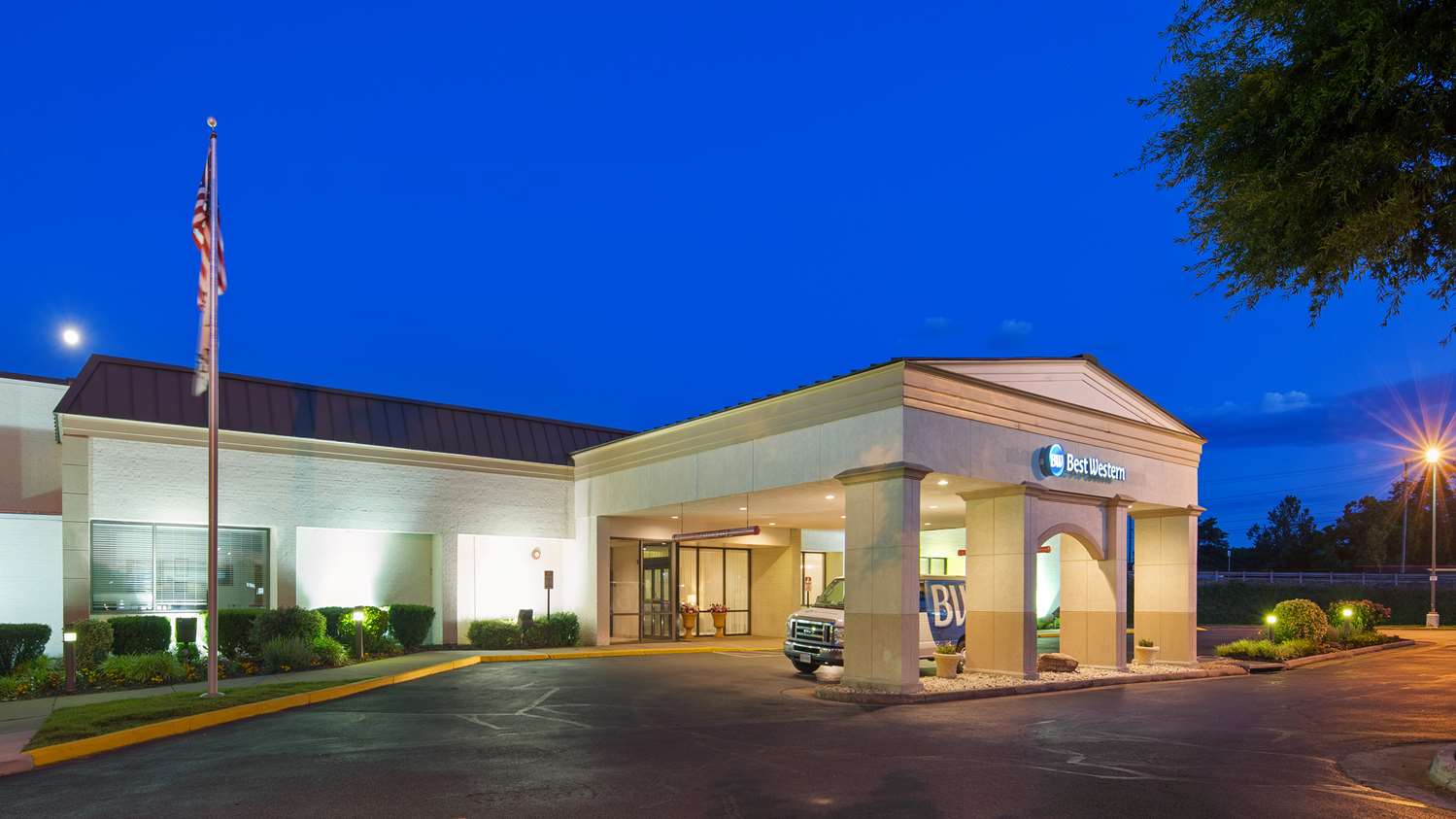 Exterior of a well-lit hotel entrance at dusk under a clear blue sky.