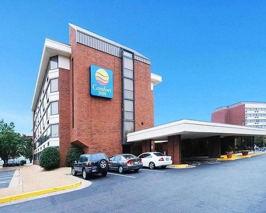 Exterior view of a Comfort Inn hotel with parked cars under a clear blue sky.