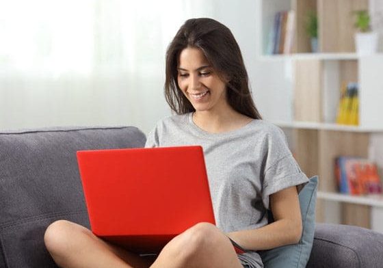 A woman smiling while using a red laptop indoors.